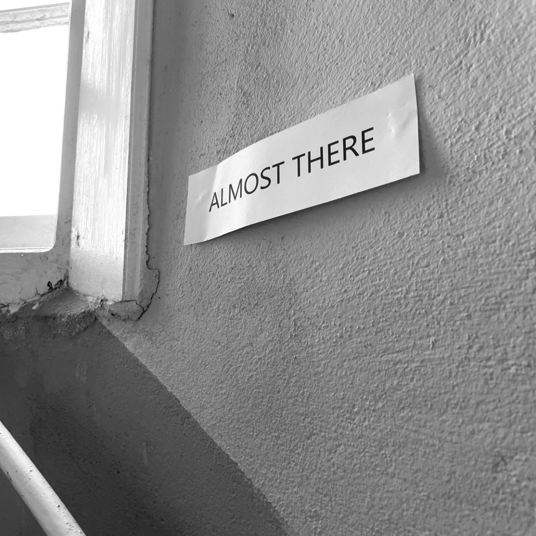 “ALMOST THERE” printed on a white piece of paper posted in a sunlit stairwell.