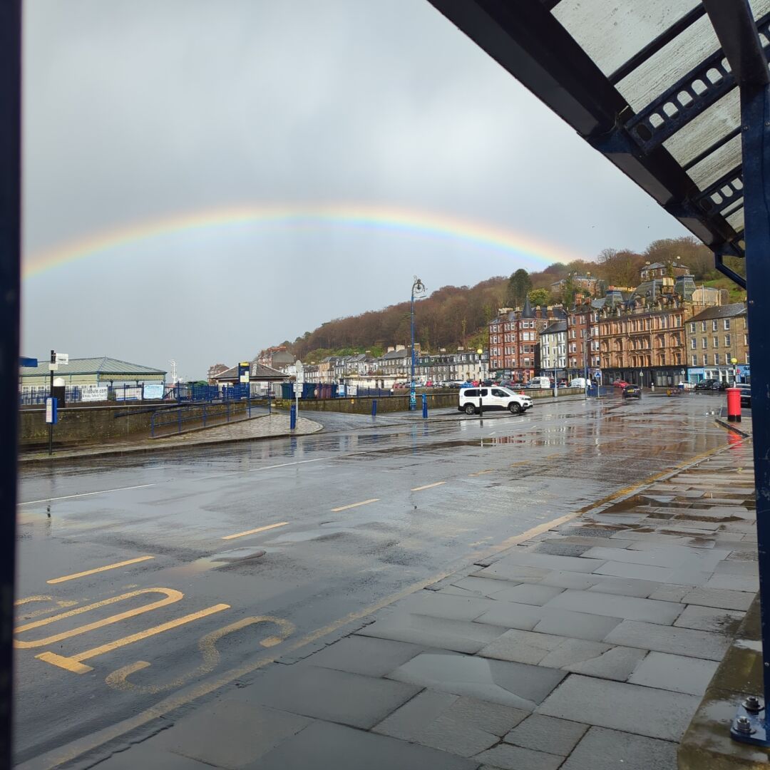 Rainbow stretching across a drenched sky, white ferry under the rainbow.