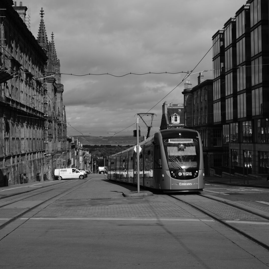 A tram travels up a quiet street with the forth behind.