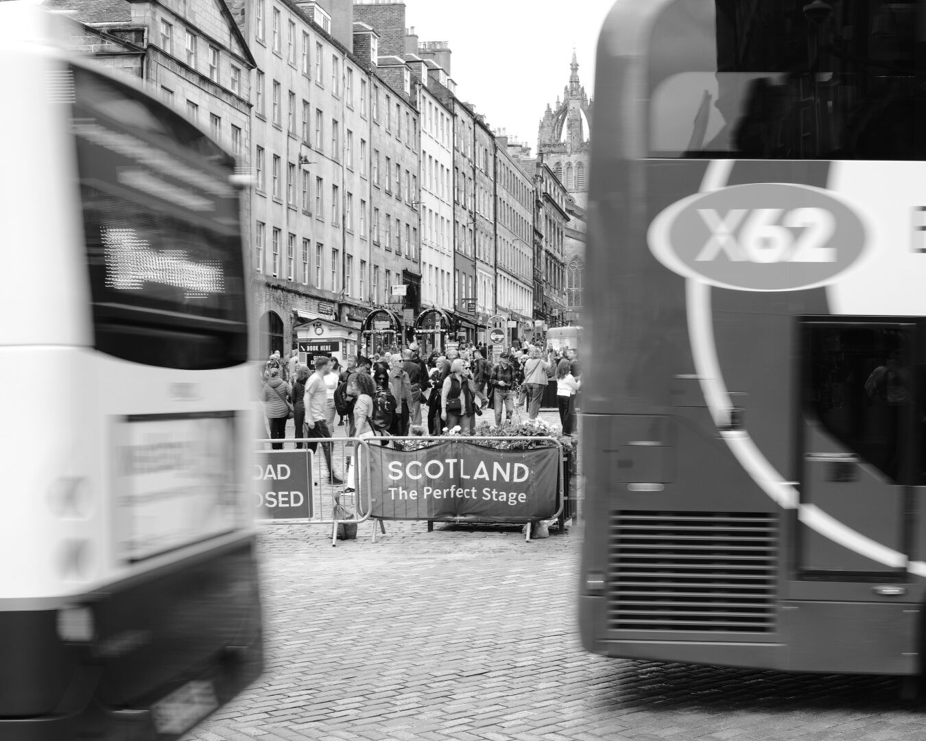 The backs of two moving buses frame a sign saying Scotland the perfect stage.