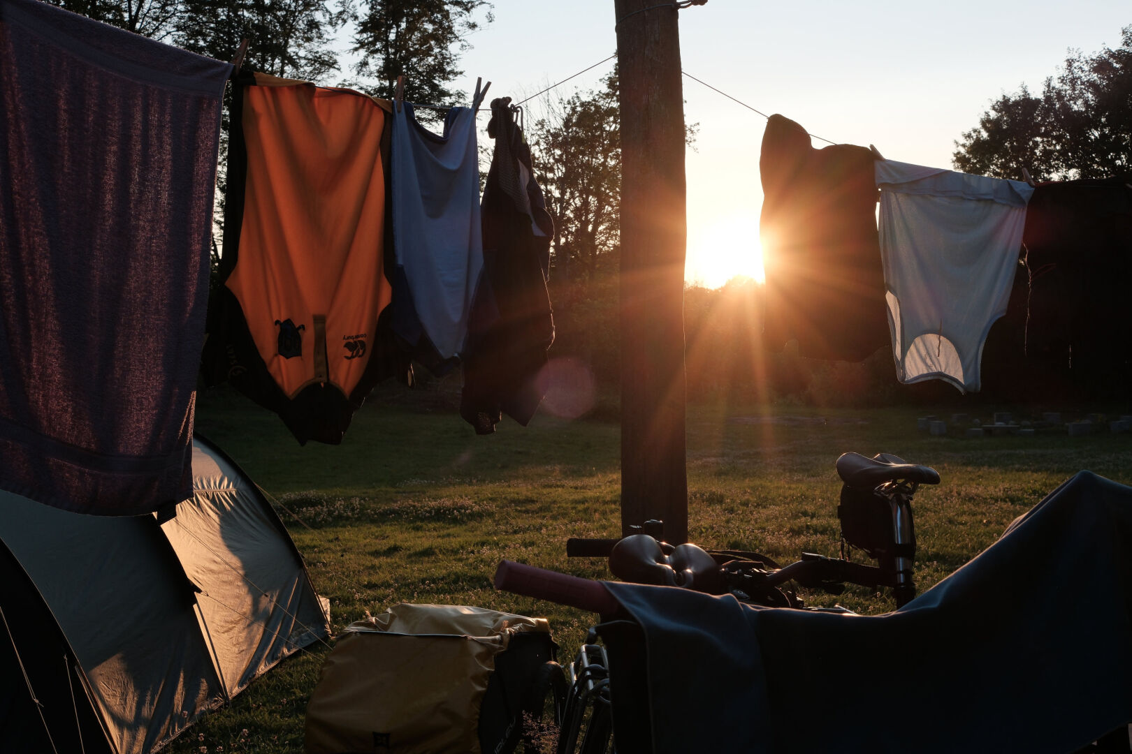 A line of washing hangs over bikes and a tent, backlit by the setting sun.