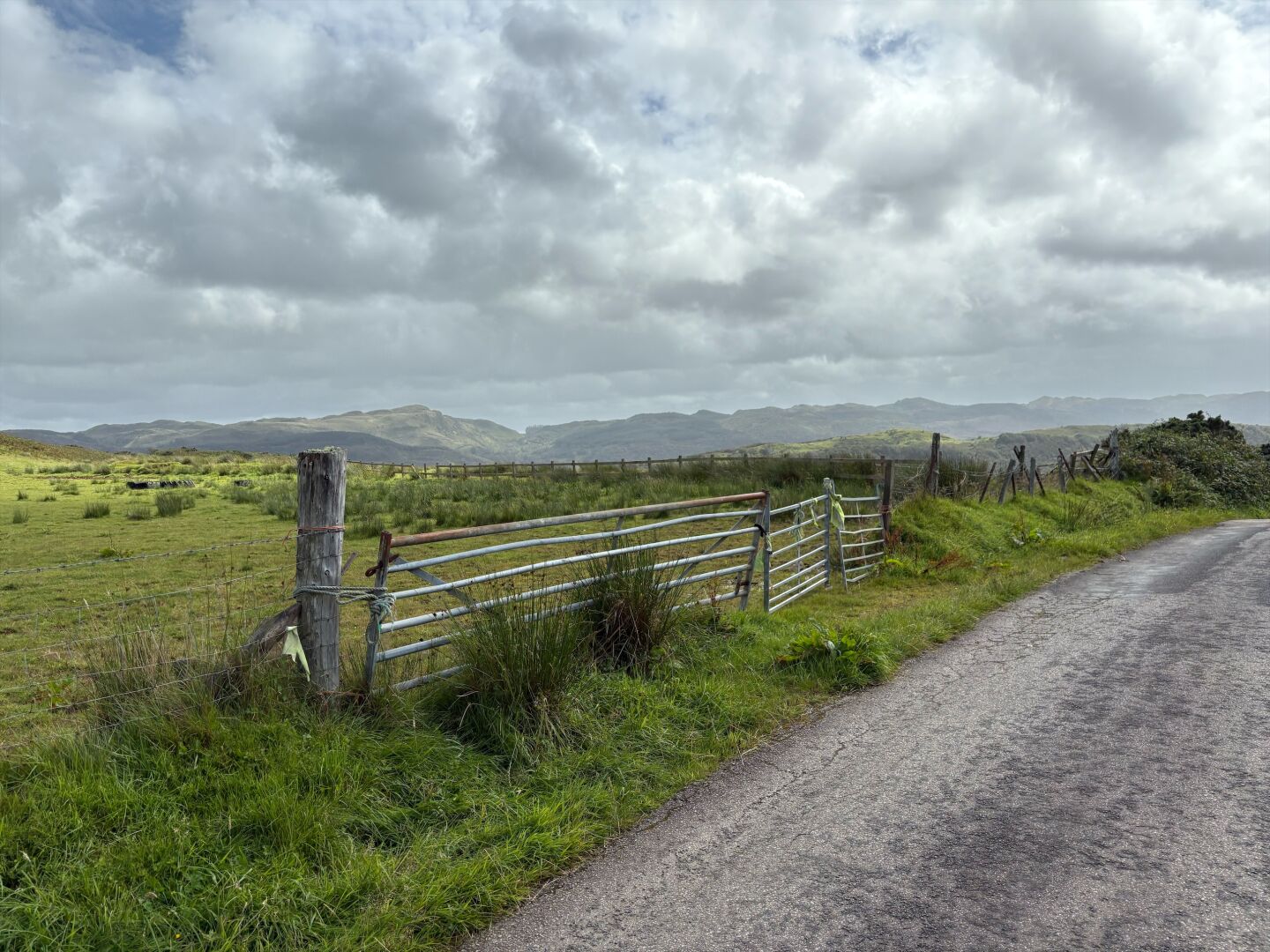 A fence, a gate, and some bumpy hills in the distance
