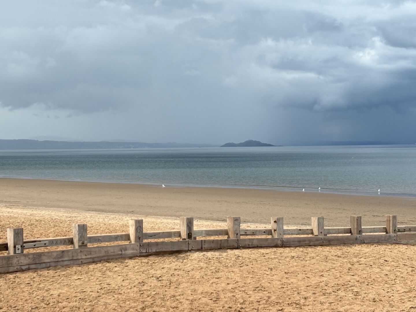 Island (Inchkeith) in the Firth of Forth as seen from beach at Portobello. The golden sand of the beach is seen in the foreground while the island seen in the distance is in deep gloom.