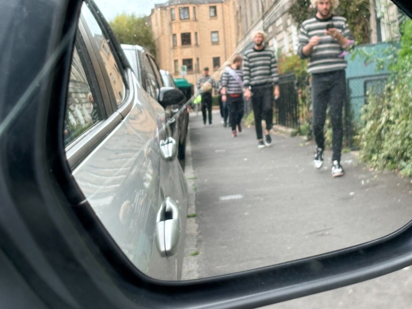 Several young males in similar attire processing along Montagy St Edina as seen in a wing mirror and then finally passing the car