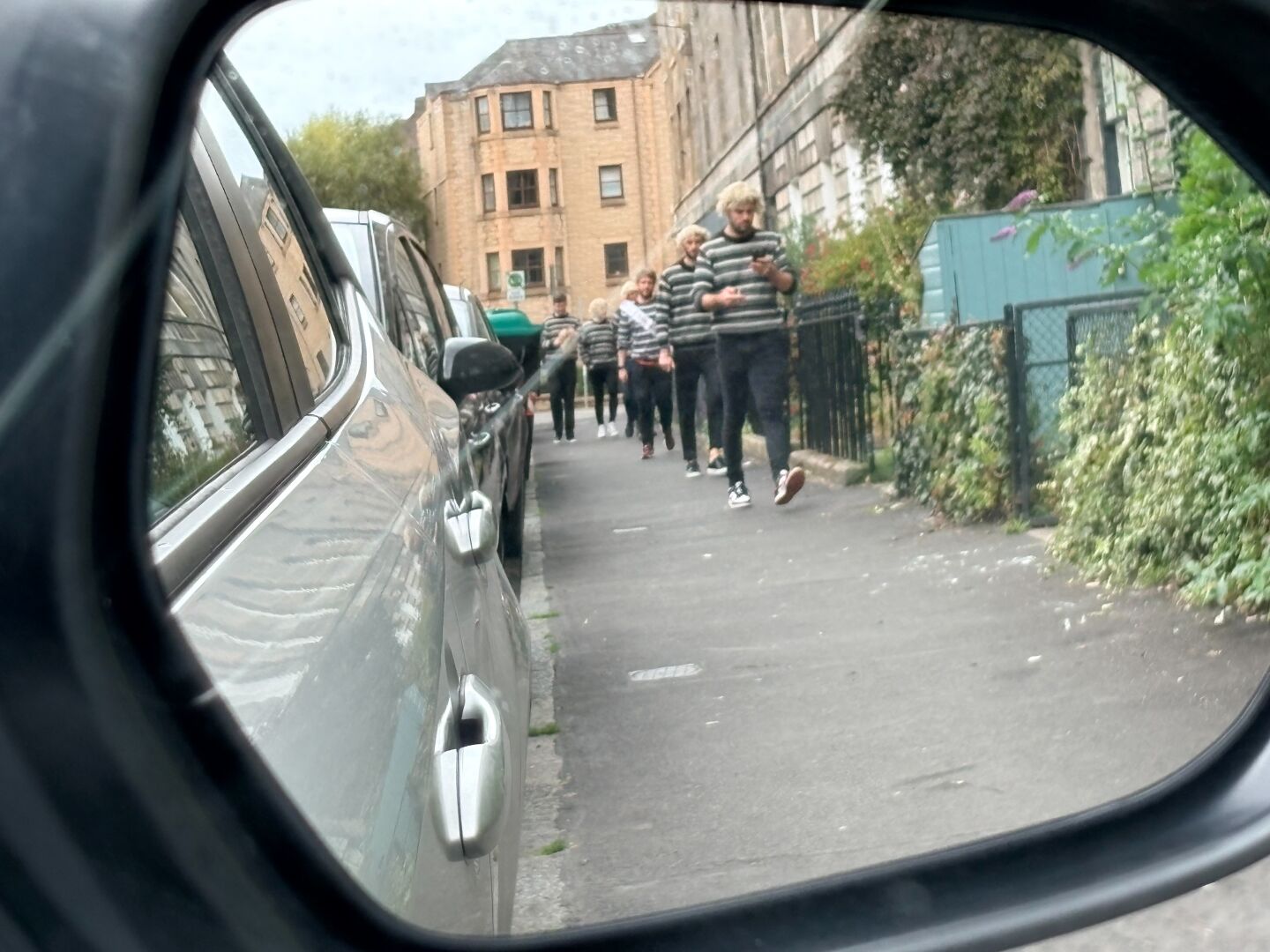 Several young males in similar attire processing along Montagy St Edina as seen in a wing mirror and then finally passing the car