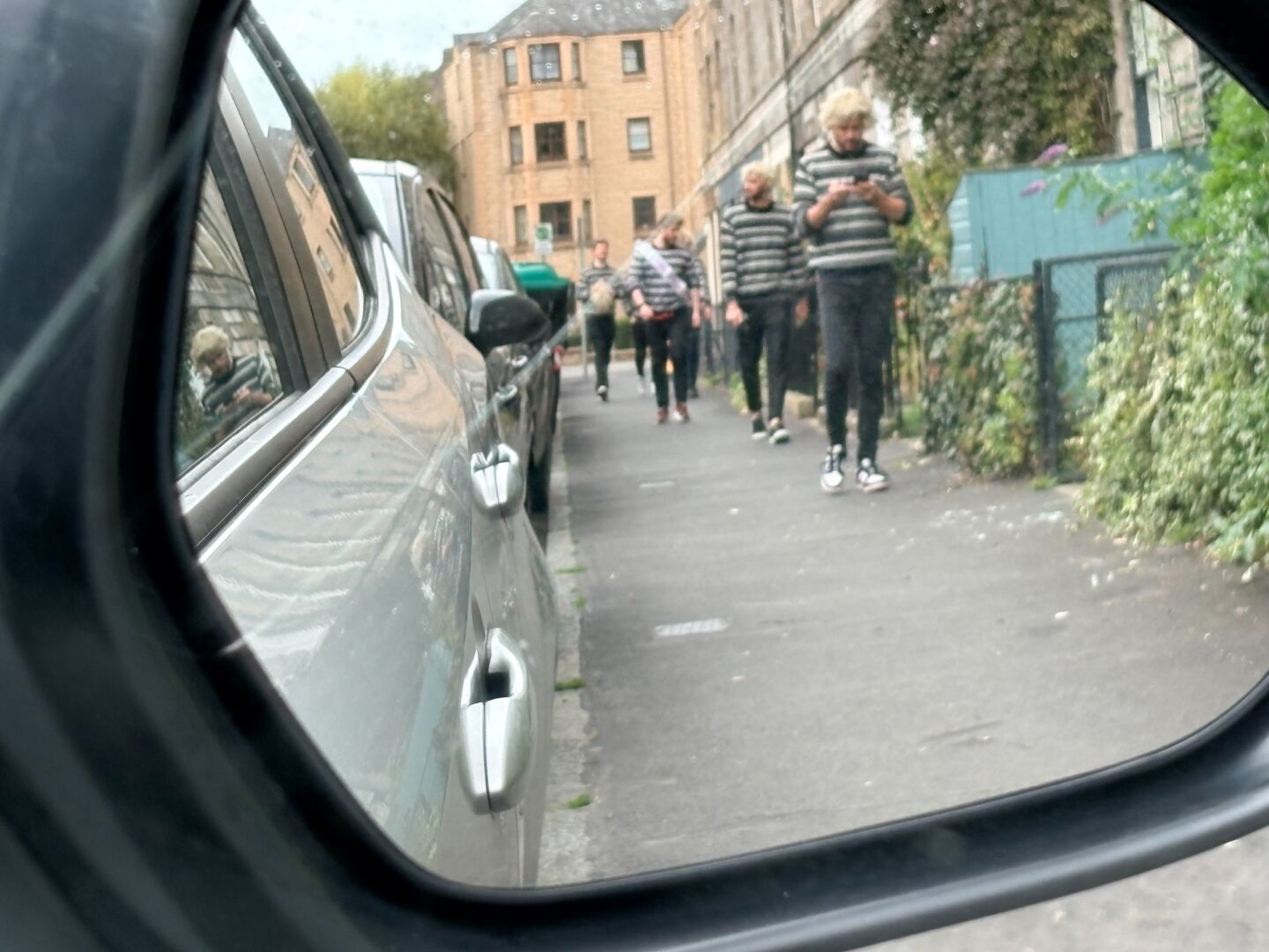 Several young males in similar attire processing along Montagy St Edina as seen in a wing mirror and then finally passing the car