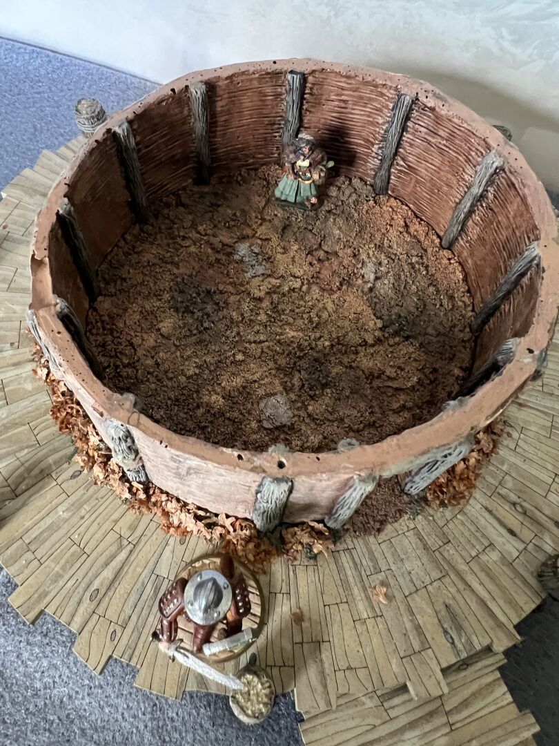 The roof has been removed from the crannog, showing the interior floor which is roughly covered with skins and heather.