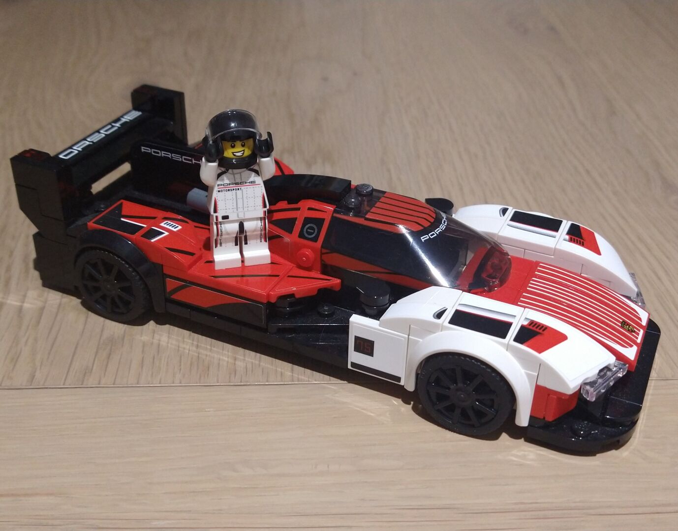 Lego minifigure of a Porsche racing driver standing on top of a Lego Porsche 963 Hypercar in which won today's race at Daytona