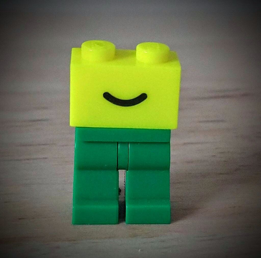 A green Lego minifigure legs with attached a laser yellow 2x1 brick with a smile printed on it. It misses the middle body part with torso and arms so it looks caricaturally strange.