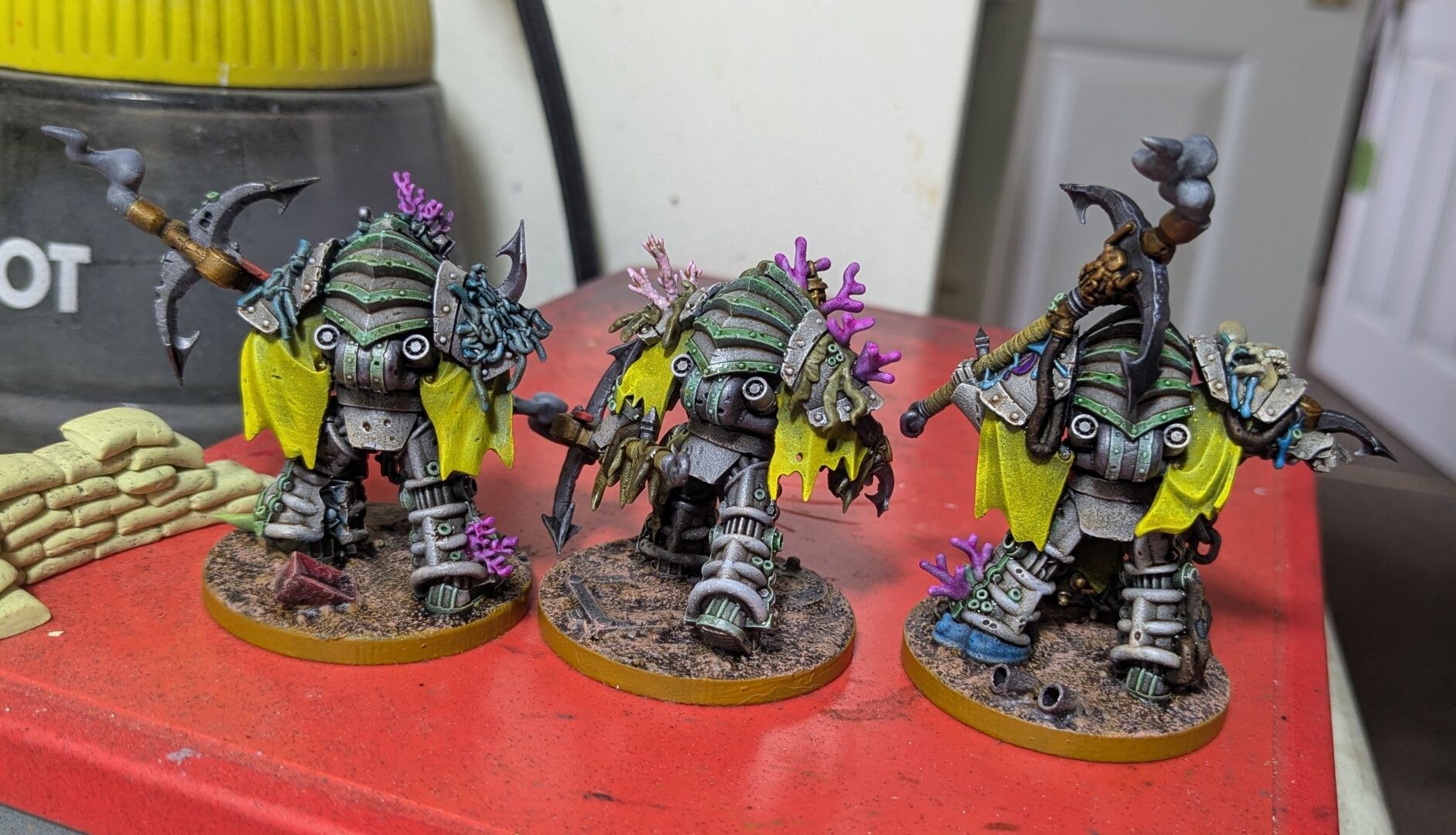 The unit of three Deep Shroud but from the back. They have decorative wing-style cape fragments hanging over their shoulders (but split so that the powerplants of their powered armour are exposed). Said capes are a bright yellow that contrasts with the drab white of their armour.