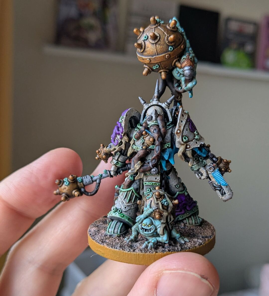 A painted wargaming miniature, specifically the Fetid minebringer from Mezgike. Essentially a sci fi human in powered armour with various sizes of sea mines, including a large one that appears to be hovering over their head. Two small creatures (dredgelings) also feature - one wearing a gas mask of sorts, clinging to the large mine, the other carrying a mine in front of the dredge marine.

The miniature is painted to have white armour with faded green edging. The whole thing looks like it has been at the bottom of the sea for a long time.