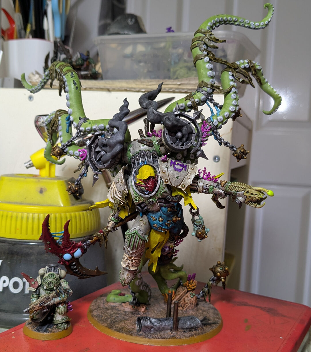 A photo of the same mini but on a desk next to a normal scale power armoured super soldier making it clear that the big guy is enormous (roughly 22cm/9" tall - about 5x the size of the other mini)